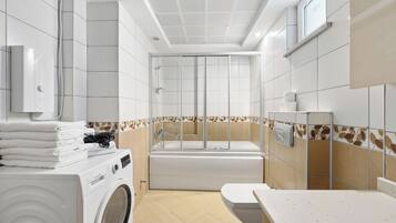 A modern bathroom with a washing machine, a bathtub, and a toilet.