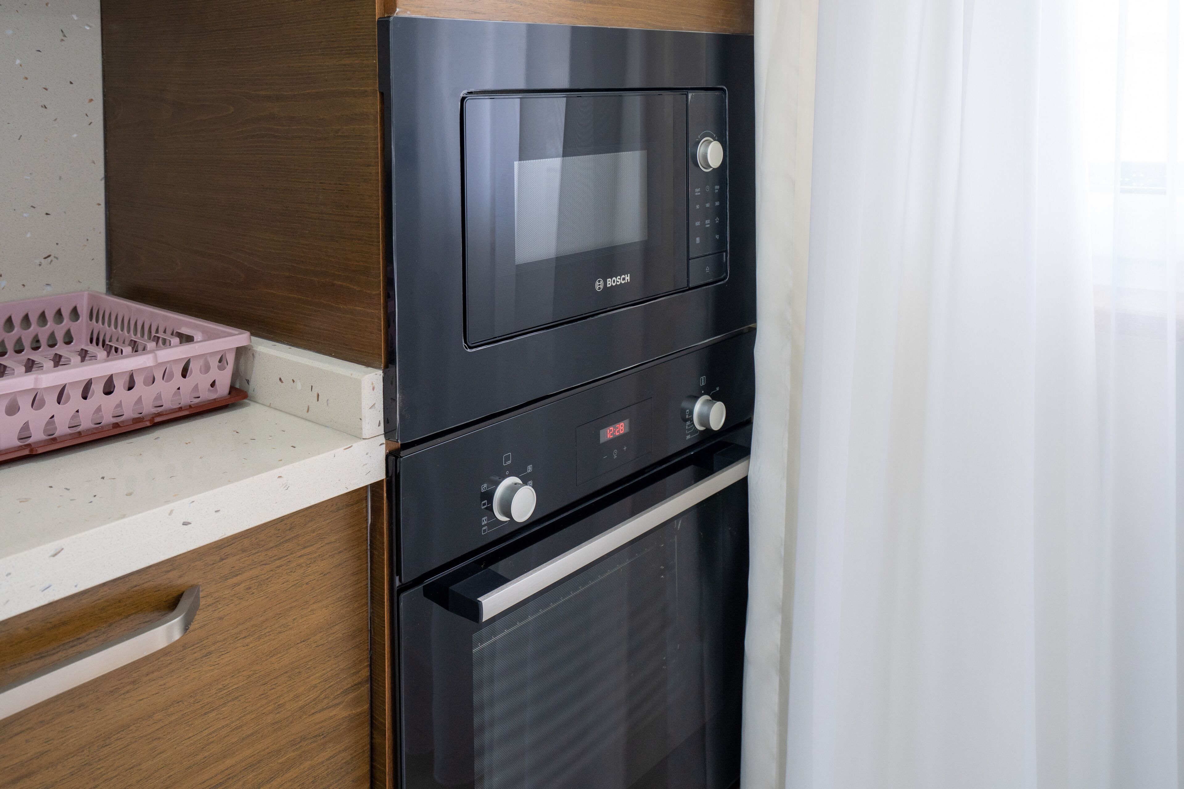 Een keuken met een Bosch magnetron en oven, een roze mand en een houten kast.