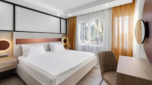 A modern hotel room with a large bed, a desk, a chair, and a television. - River Park Residence Lara (Antalya)