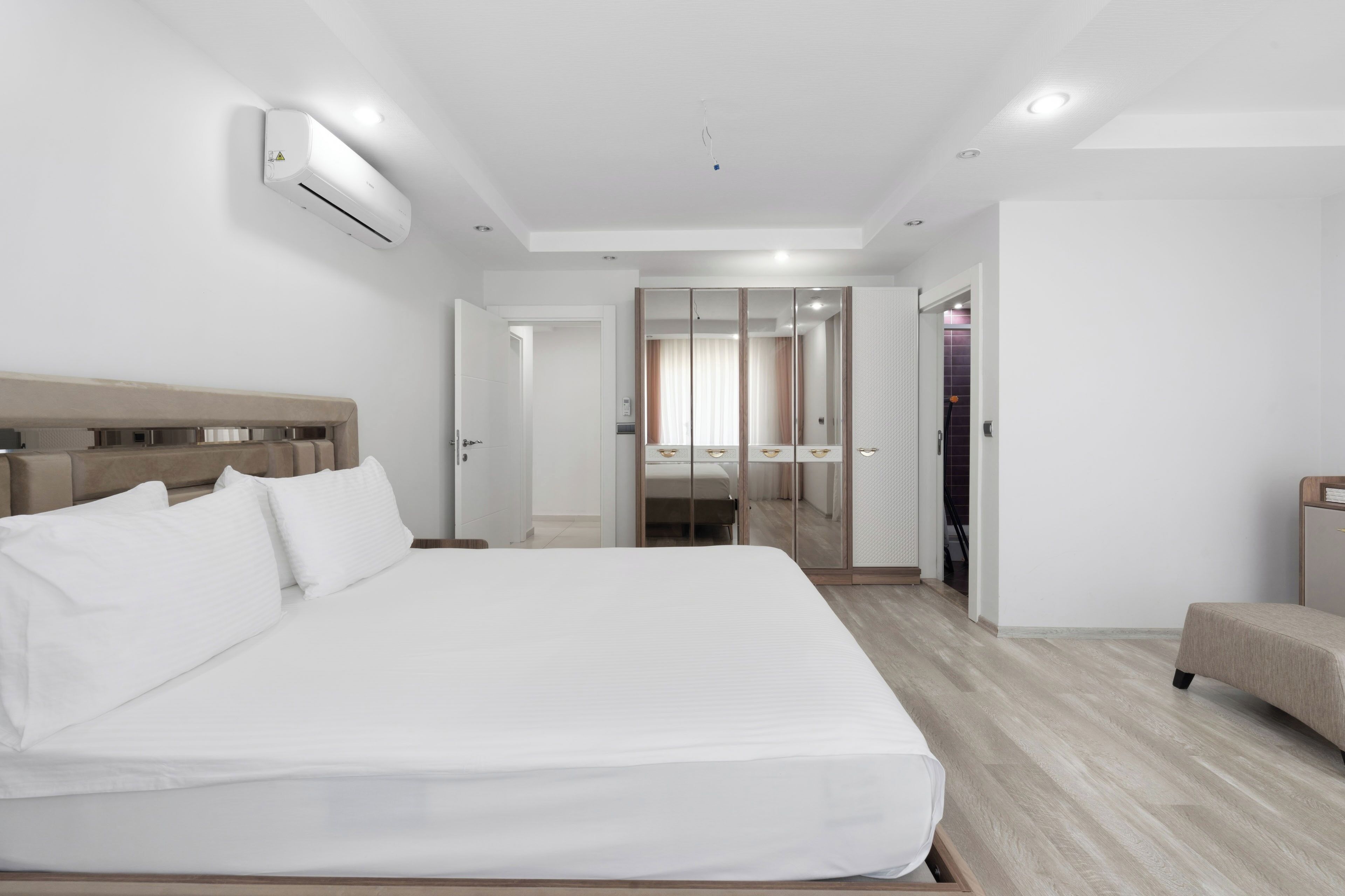 A modern hotel room with a large bed, a bedside table, a wardrobe, and a seating area.