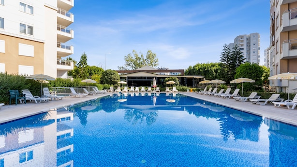 A swimming pool with lounge chairs and umbrellas, surrounded by apartment buildings. - River Park Residence Lara (Antalya)