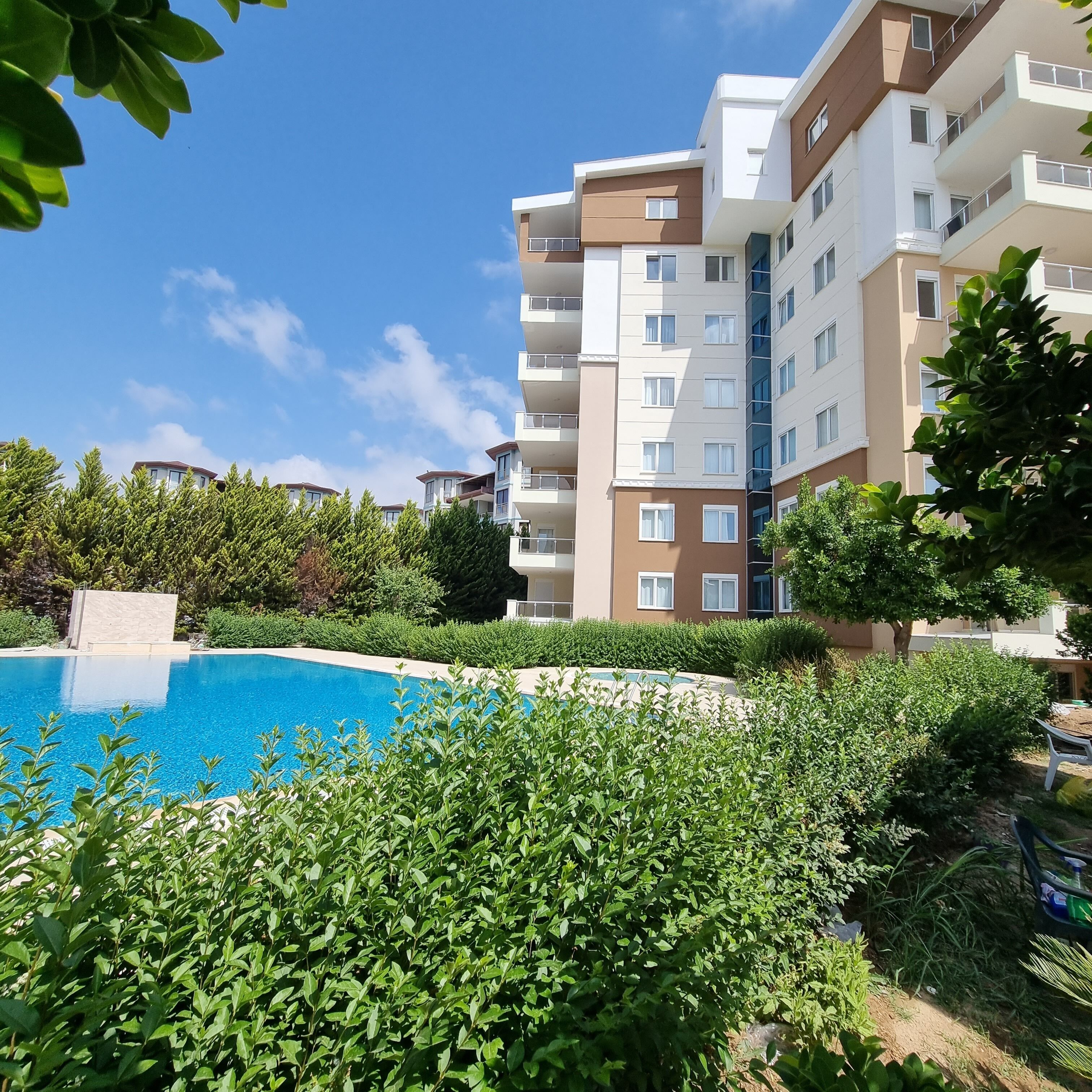 A modern apartment building with a swimming pool surrounded by lush greenery.