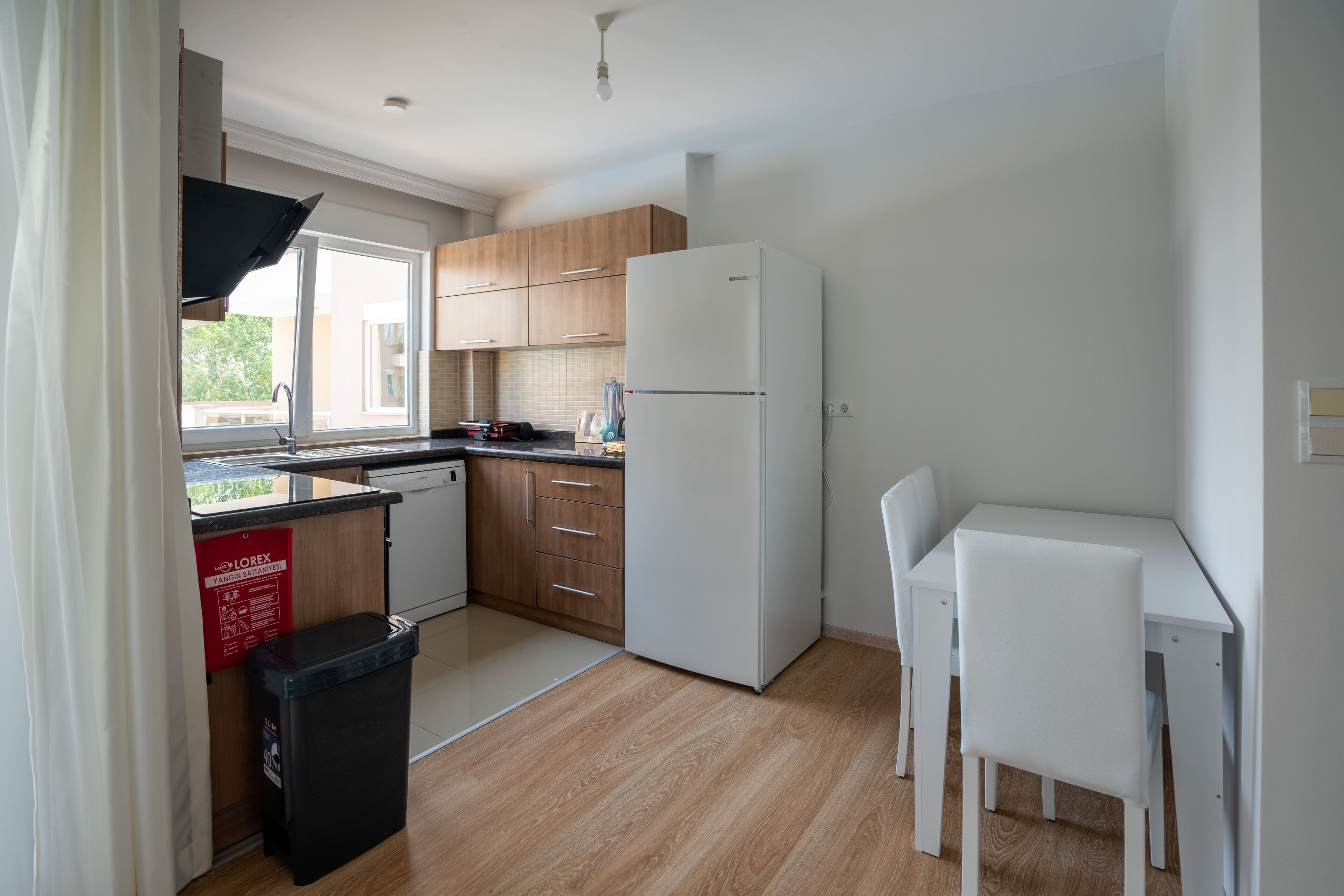 A modern kitchen with wooden cabinets, a white refrigerator, a sink, and a dining area with a white table and chairs.