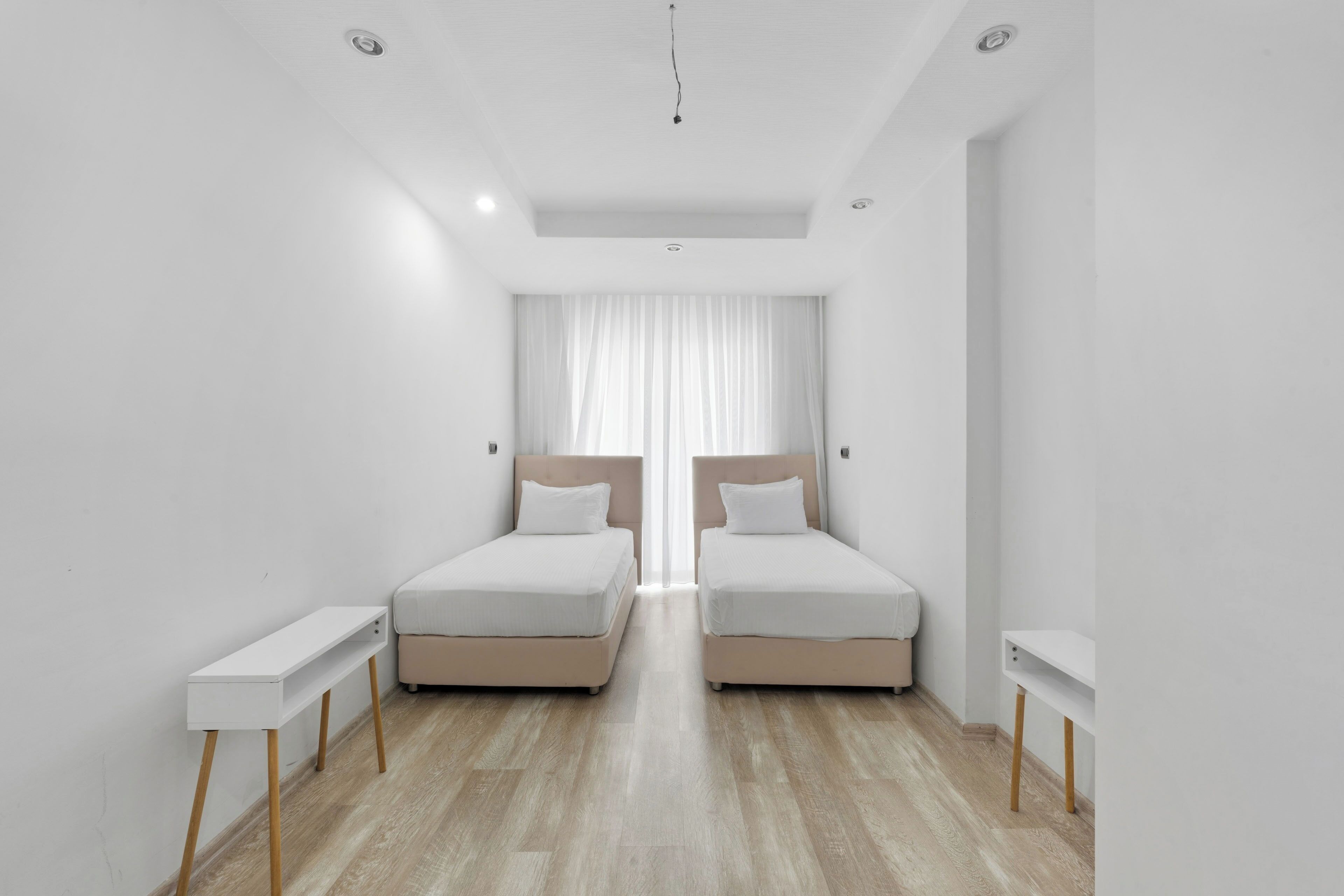 Ein modernes Schlafzimmer mit zwei Betten, einem kleinen Nachttisch und einem großen Fenster mit Vorhängen.