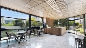 A modern indoor space with a large open area featuring a marble floor, a wooden ceiling, and large windows offering a view of the outdoors. - River Park Residence Lara (Antalya)