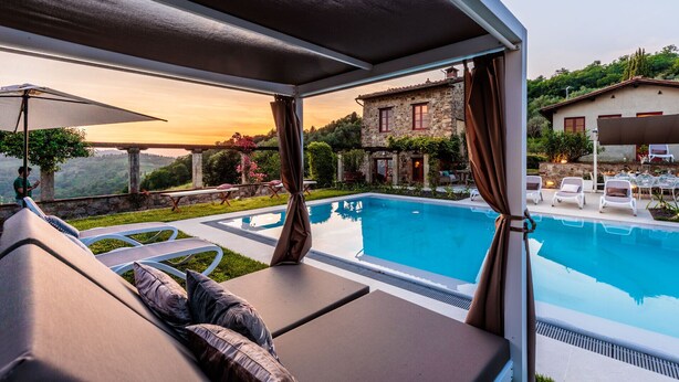 Ein Poolbereich mit Liegestühlen und einem dahinterliegenden Steinhaus.