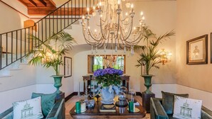 Eine prachtvolle Treppe mit einem Chandelier, ein Holztisch mit Dekoration und grüne, gepolsterte Sofas.