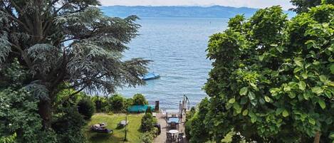 A view of a lake with a boat docked on the shore, surrounded by lush greenery and a clear sky.