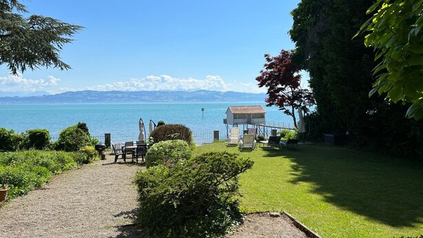 A coastal view with a grassy area, a small building, and a clear sky. - Villa Gerster (Wasserburg am Bodensee)