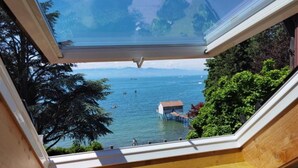 A view from a window with a wooden ledge and a skylight, overlooking a body of water with boats and a small dock. - Villa Gerster (Wasserburg am Bodensee)