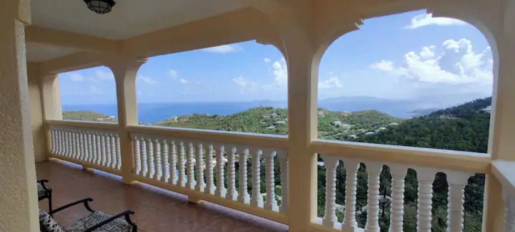 A balcony with a white balustrade, a view of the sea, and a mountainous landscape.