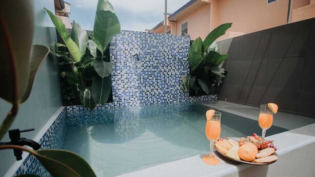 Ein Poolbereich mit gefliesten Wänden und Pflanzen, ein Tablett mit zwei Getränken und ein Obstteller.