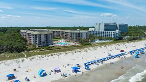 A beachfront hotel with multiple buildings, a pool area, and a sandy beach with umbrellas and sun loungers. - Fifth Floor Villamare unit with lots of updates! (Hilton Head)