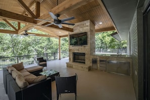 An outdoor patio with a stone fireplace, wicker furniture, and a ceiling fan.