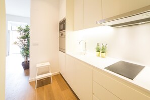 A modern kitchen with white cabinetry, a built-in oven, and a black induction cooktop.