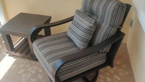 Uma cadeira com almofada listrada e uma pequena mesa ao lado, ambas com estrutura escura, sobre piso de azulejos.