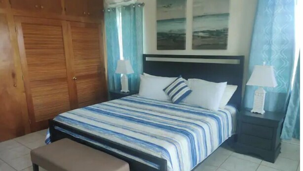 Quarto bem arrumado com cama, mesas de cabeceira, um banco e um guarda-roupa.