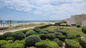 A coastal view with a beach, a well-maintained garden, and modern buildings. - STUDIO WITH SEA VIEW TERRACE FACING THE BEACH (Le Barcarès)