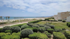 A coastal view with a beach, a well-maintained garden, and modern buildings. - STUDIO WITH SEA VIEW TERRACE FACING THE BEACH (Le Barcarès)