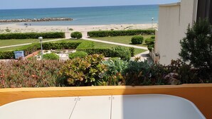 A balcony with a white table and two chairs, overlooking a beach with a clear sky. - STUDIO WITH SEA VIEW TERRACE FACING THE BEACH (Le Barcarès)
