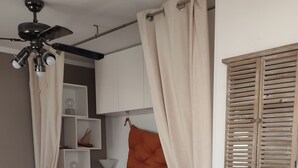 A cozy bedroom with a bed, a ceiling fan, a window with shutters, and a small white table. - STUDIO WITH SEA VIEW TERRACE FACING THE BEACH (Le Barcarès)