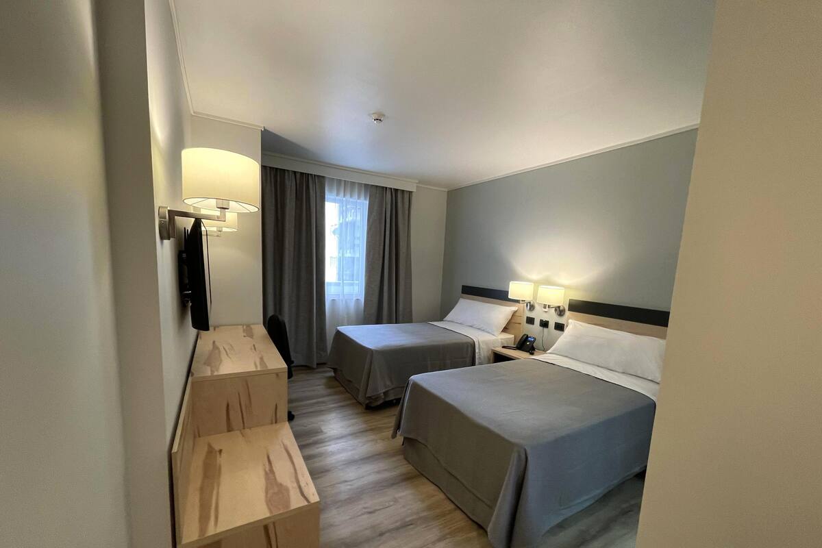 Een hotelkamer met twee bedden, een bureau en een stoel. Op het bureau staan twee bedlampjes en een telefoon.