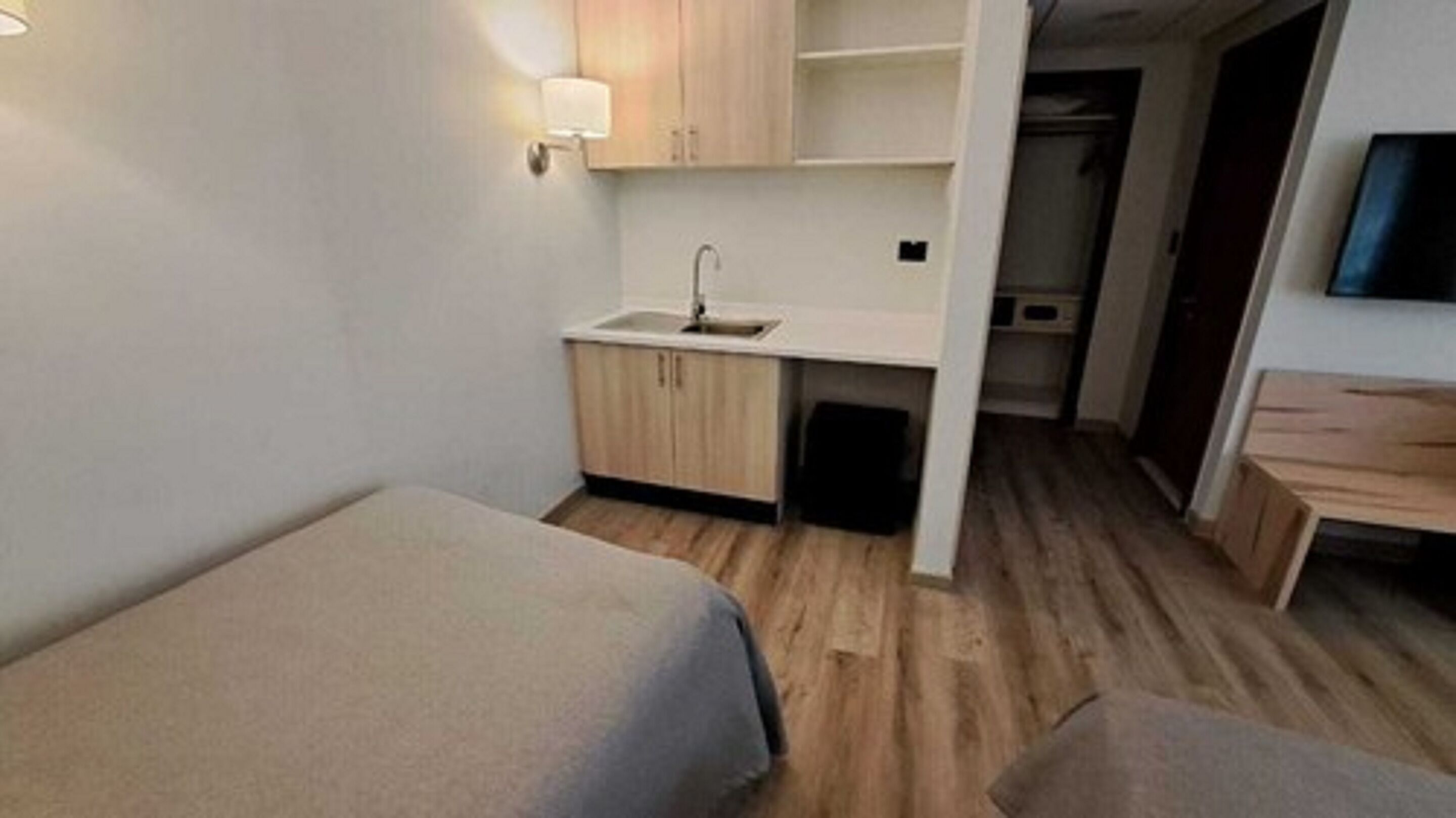 Ein kleines Hotelzimmer mit zwei Einzelbetten, einer kompakten Küchenzeile und Holzboden.
