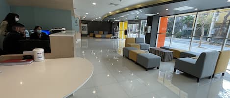 A modern reception area with a curved reception desk, seating area with sofas and armchairs, and large windows offering a view of the street.