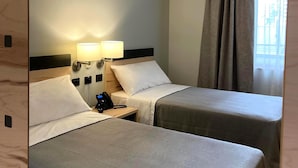 Une chambre d’hôtel avec deux lits, une lampe de chevet, un téléphone et une fenêtre avec des rideaux.