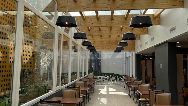 Un vaste espace intérieur doté de poutres en bois et de grandes fenêtres, aménagé avec de nombreuses tables et chaises disposées pour les repas.