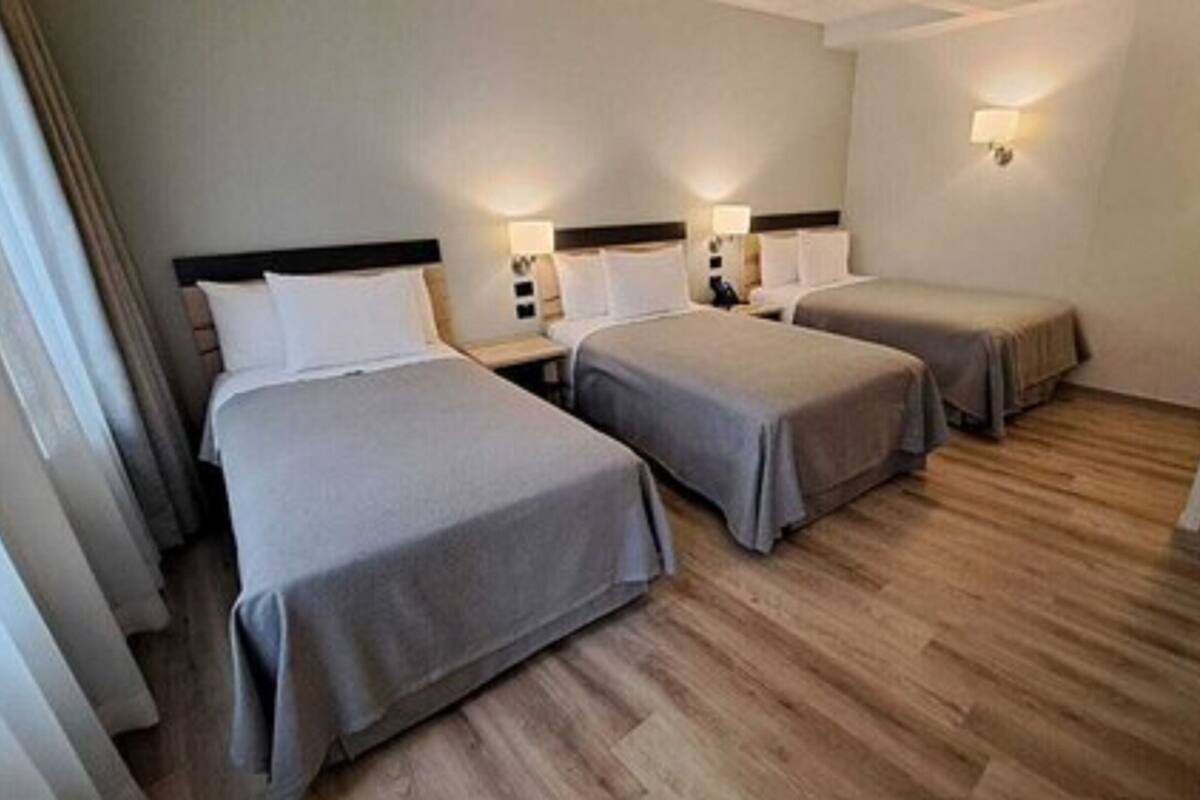 Een hotelkamer met twee eenpersoonsbedden, een houten vloer en een nachtkastje met een lamp.
