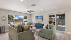 A living room with a ceiling fan, a large window, a blue cabinet, and a sliding glass door leading to an outdoor area. - Pool home,Pet friendly, 5 mins drive to Siesta Key (Sarasota)