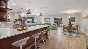 A modern kitchen with a central island, bar stools, pendant lighting, and a dining area with a table and chairs. - Pool home,Pet friendly, 5 mins drive to Siesta Key (Sarasota)