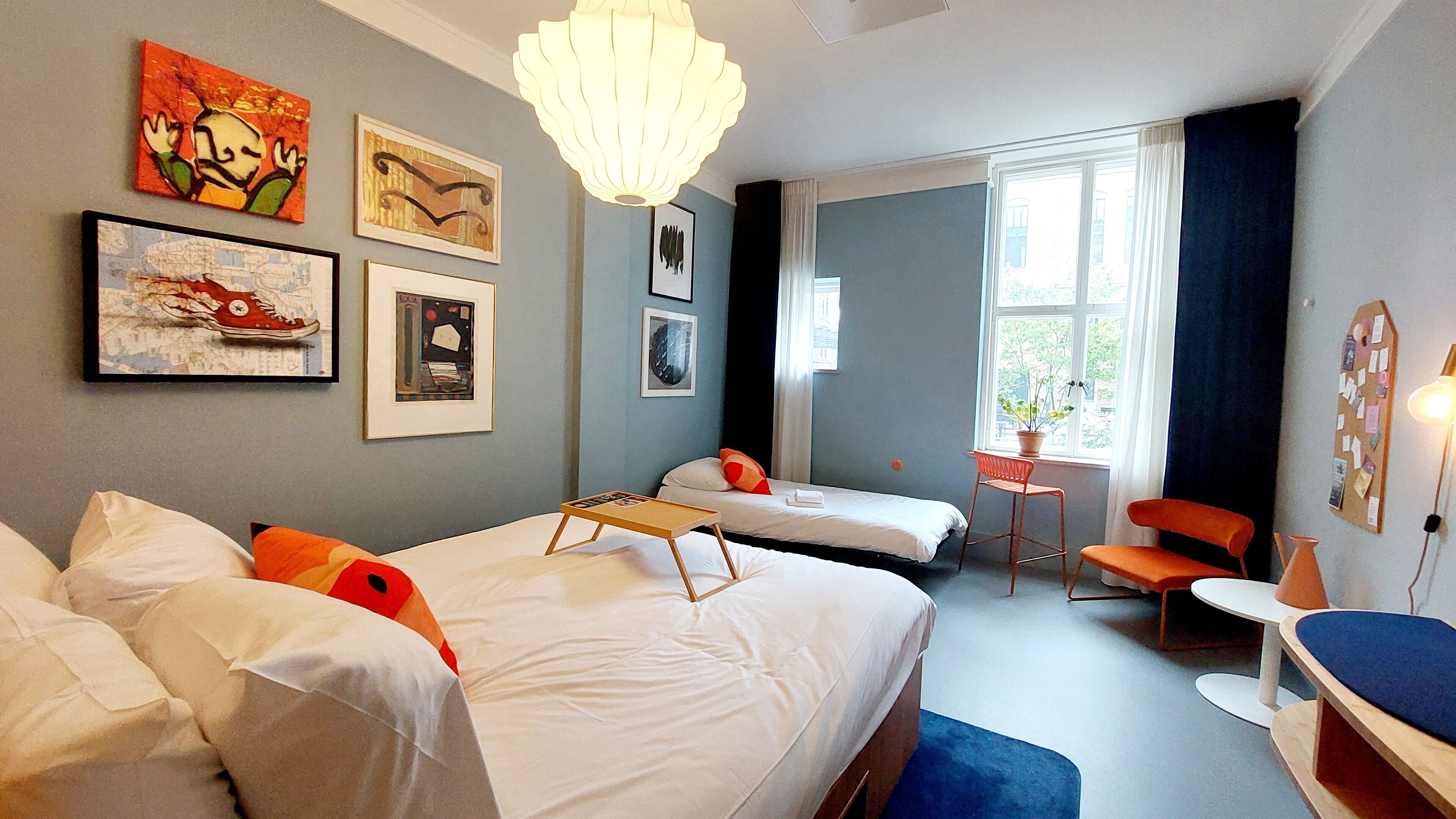Een hotelkamer met twee bedden, een bureau, een stoel en kunstwerken aan de muren.