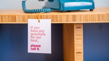 A blue rotary phone on a wooden table with a tag that reads "If you have any questions for our host, please call 9."