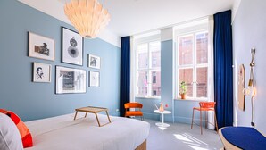 Una habitación de hotel moderna con una cama grande, una mesita, dos sillas y una ventana con vistas a la ciudad.