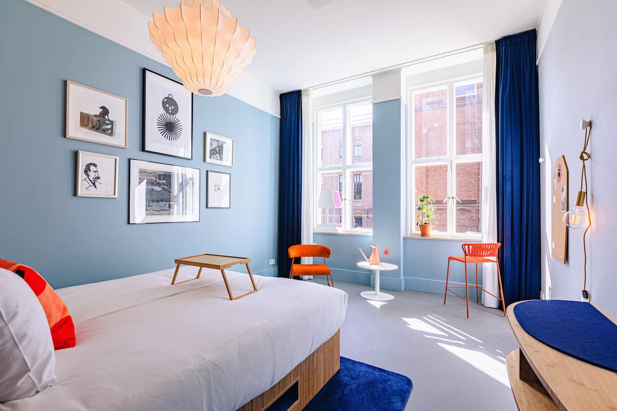A modern hotel room with a large bed, a small table, two chairs, and a window with a view of the city.