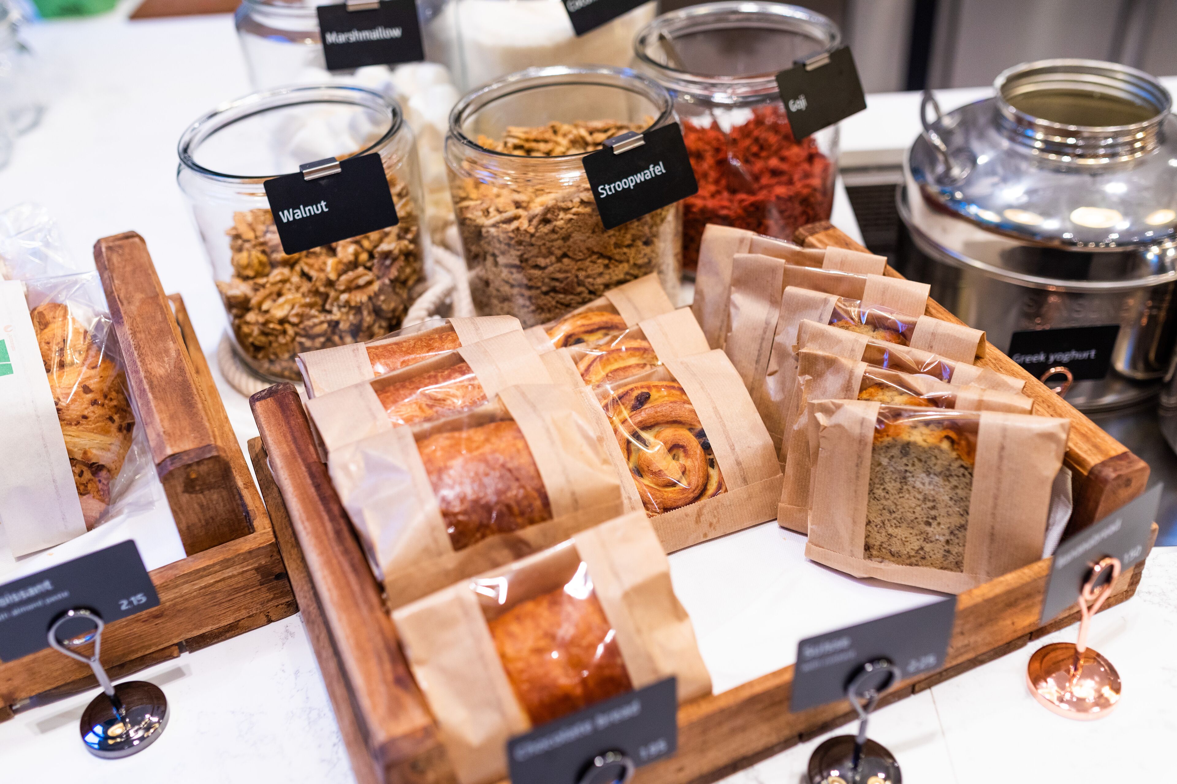 Variedad de alimentos, como granola, galletas y pan, expuestos en recipientes transparentes y bolsas de papel.