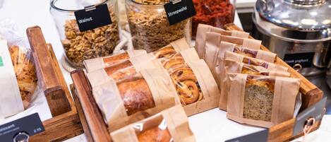 Variedad de alimentos, como granola, galletas y pan, expuestos en recipientes transparentes y bolsas de papel.