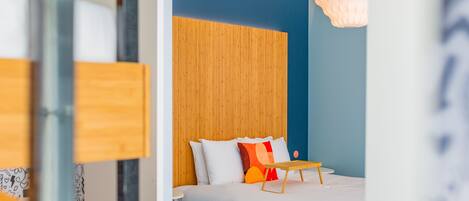 Une chambre à coucher moderne avec une tête de lit en bois, un lit recouvert de linge de lit blanc et une petite table en bois.