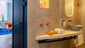 Un baño moderno con una puerta oscura, un lavabo blanco con cuenco, un espejo con luz y un perchero.
