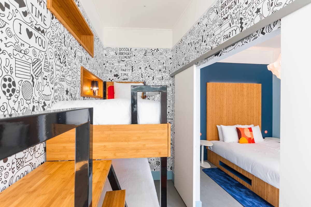 A compact room with a bunk bed, a small bedside table, and a wall decorated with doodle-style drawings.