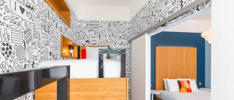 Une petite chambre avec un lit superposé, une petite table de chevet et un mur décoré de dessins enfantins.