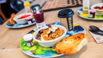 A breakfast setting with a bowl of cereal, a croissant, a coffee cup, and a bottle of smoothie.