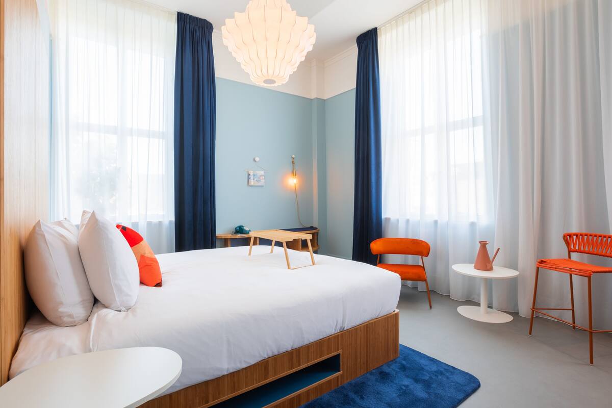A modern hotel room with a large bed, two chairs, a small table, and a desk.