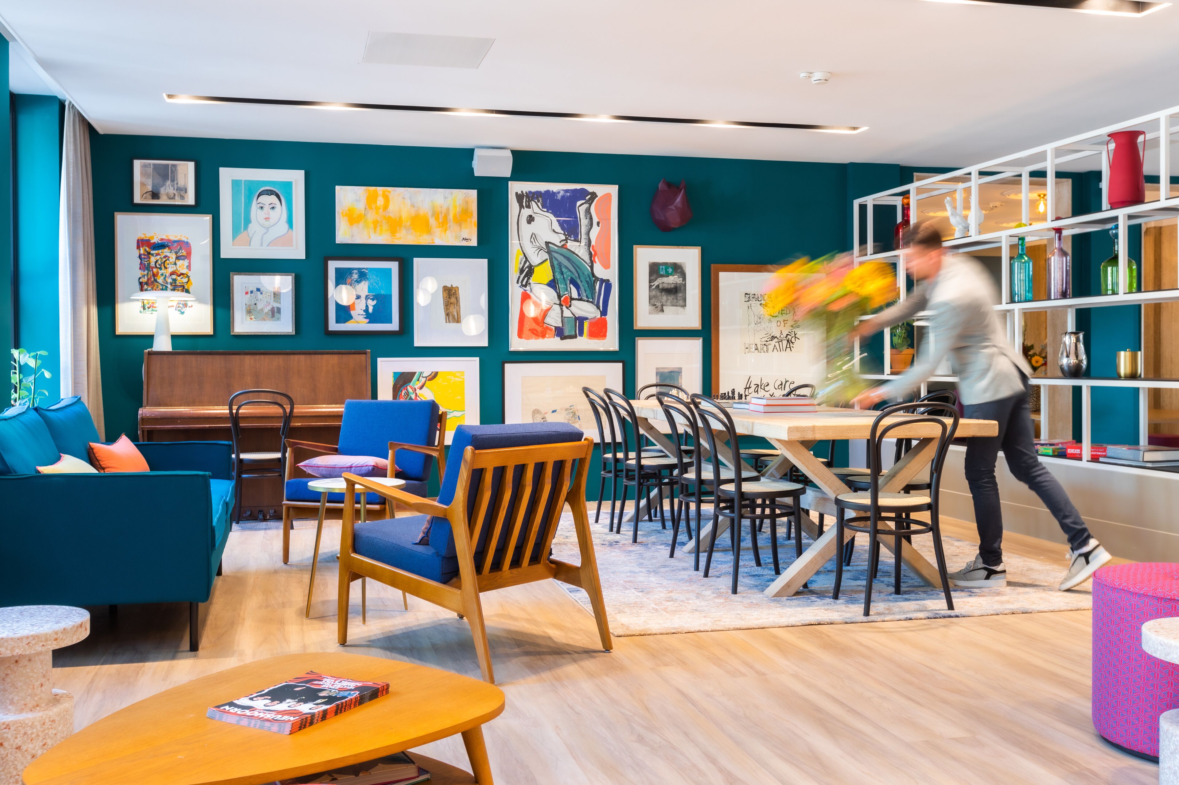 Un interior moderno con paredes verde azulado, muebles de madera y una variedad de obras de arte enmarcadas.