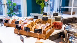 Un bufé con recipientes etiquetados de diversos alimentos como pan de chocolate, croissant, stroopwafel, nuez, goji y coco.