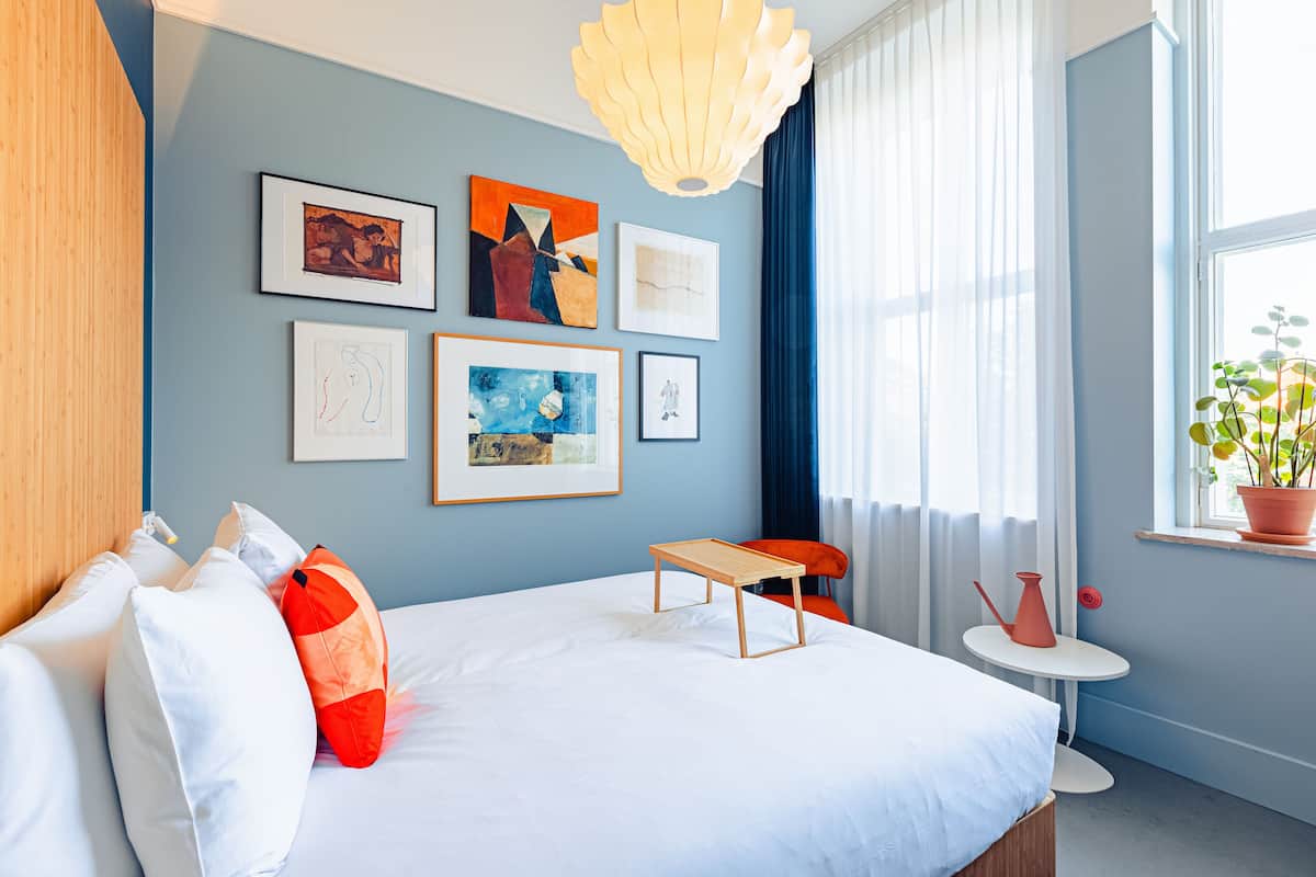 A modern hotel room with a large bed, a small table, and artwork on the wall.