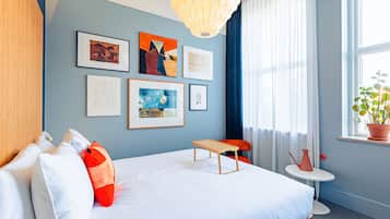 A modern hotel room with a large bed, a small table, and artwork on the wall.