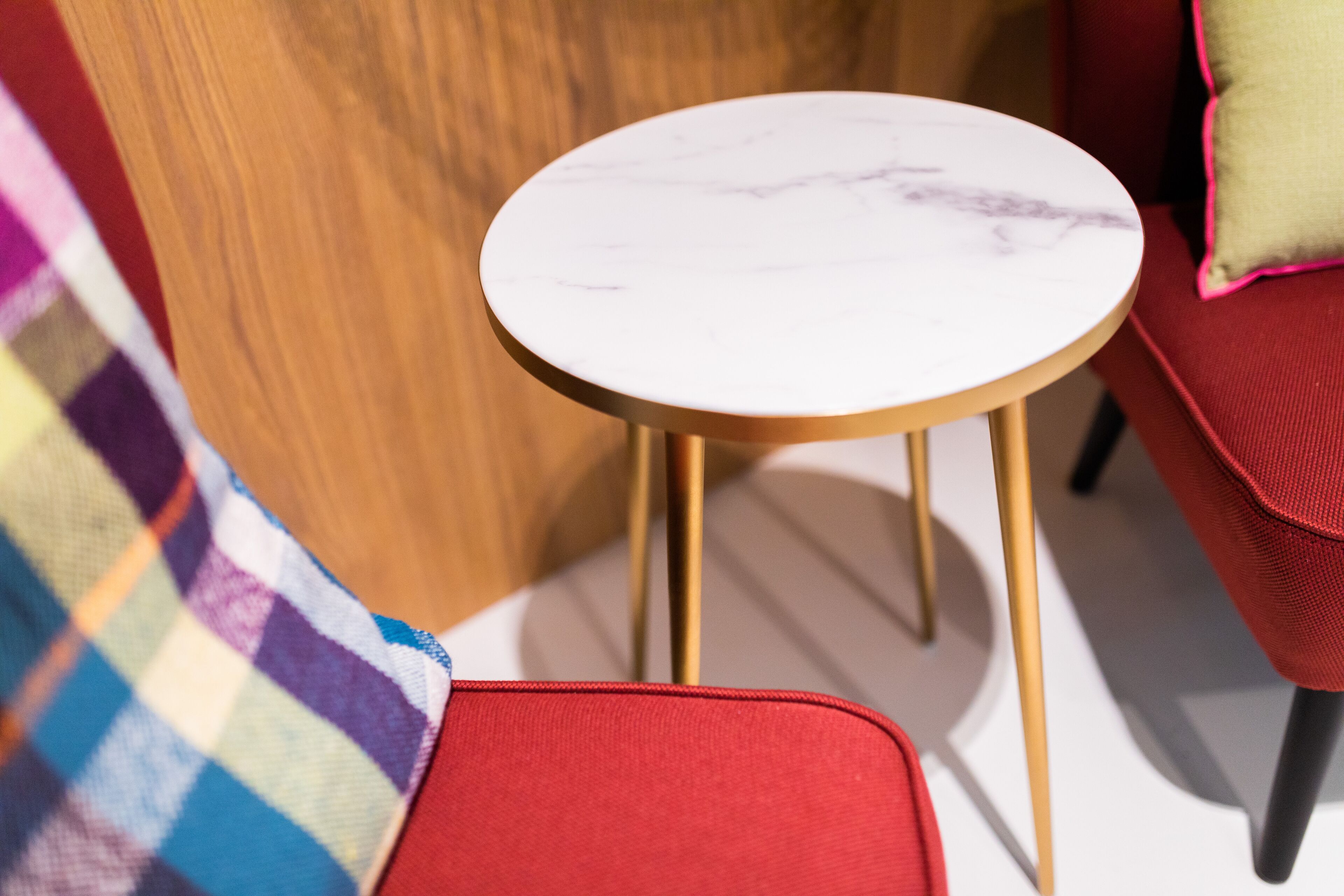 Een klein rond tafeltje met een witte marmeren blad en gouden poten, geplaatst op een rode stoel.